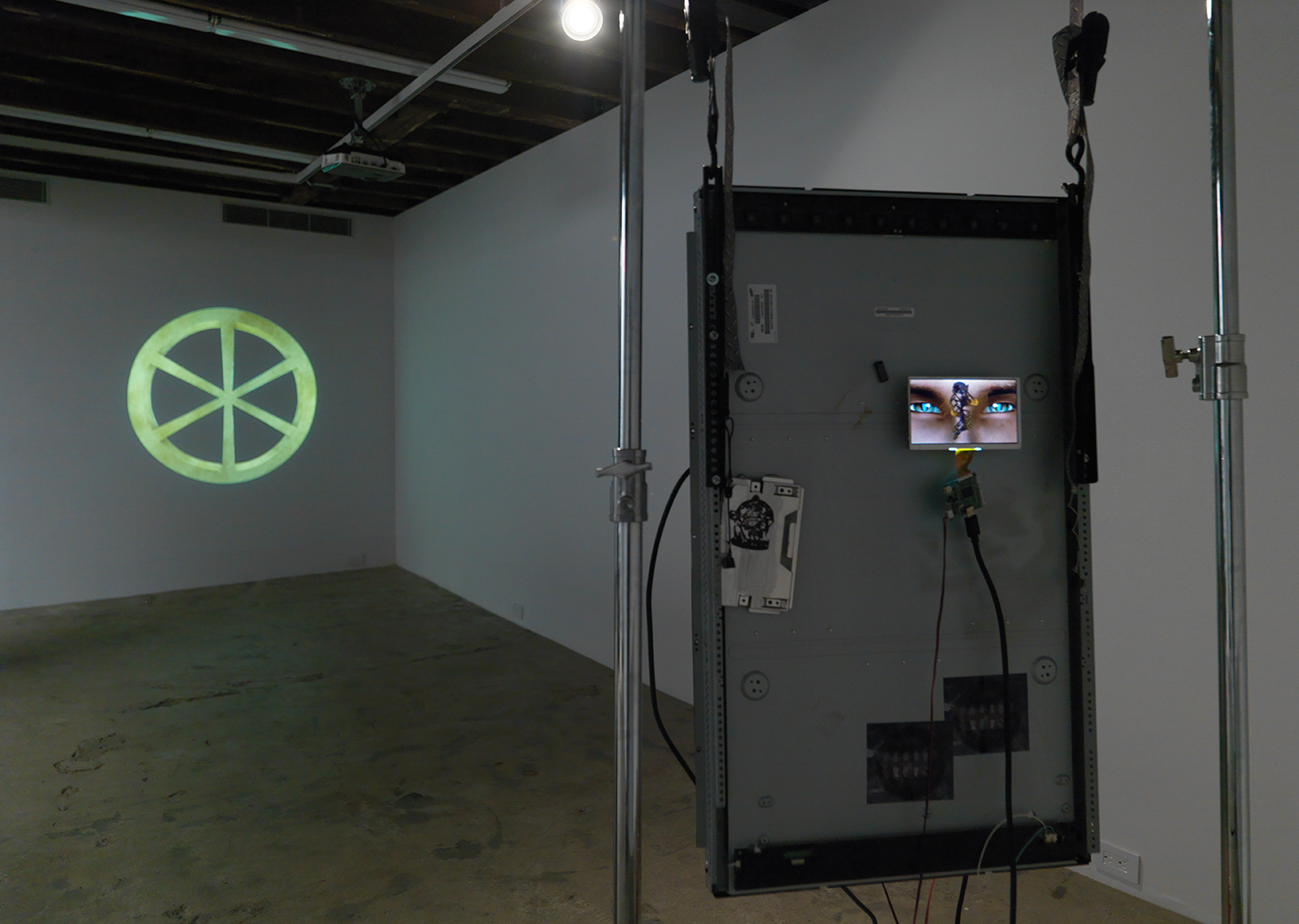 Theodore Darst, And How To Find The Real One (Alternate installation view), 2017, acrylic on Panasonic HD Monitor, Vinyl Sticker, 3 HD Video Loops, C Stand, Sandbags, dimensions variable; Theodore Darst, WROL (Got The Life), 2017, single channel HD video projection, 2:47 minutes, dimensions variable. Edition of 3 + 2 Artist Proofs